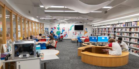 St. George Library Center Teen Center, featuring teens using computers and sitting at work tables. A colorful mural fills the wall in the background, with shelves of books on the adjacent wall.
