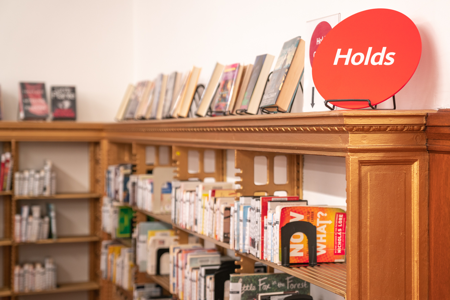 Image of wooden shelves full of books with a sign that says "Holds".